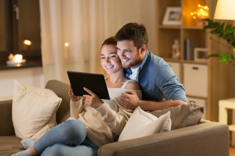 Junges Paar sitzt entspannt auf dem Sofa und nutzt gemeinsam ein Tablet im Wohnzimmer.