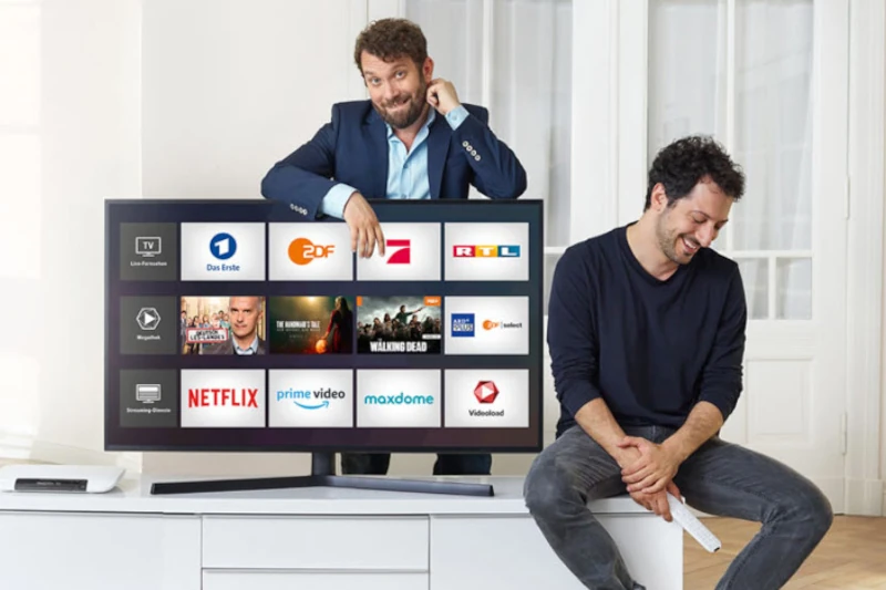 Zwei Männer präsentieren einen Smart-TV mit beliebten Streaming- und Mediathek-Apps.