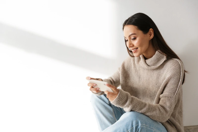 Junge Frau sitzt entspannt mit Smartphone und lächelt, Freizeit und Kommunikation zuhause.