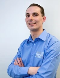 Mann im blauen Hemd mit Firmenlogo steht lächelnd vor weißem Hintergrund, Servicepersonal.