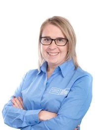 Frau mit Brille und blauem Hemd lächelt freundlich, professionelle Mitarbeiterin im Büro.