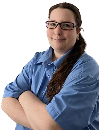 Frau im blauen Arbeitshemd mit Brille steht selbstbewusst und verschränkt die Arme.