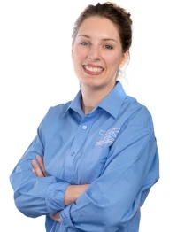 Junge Frau im blauen Hemd mit verschränkten Armen lächelt freundlich in die Kamera.